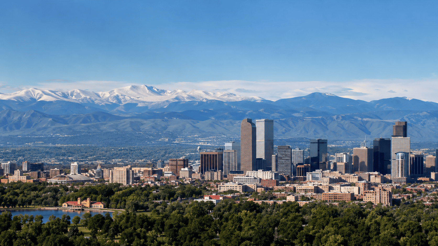 Downtown Denver skyline with snow-capped Rocky Mountains, City Park lake and pavilion in the foreground, backdrop for Colorado motivational speaker Dr. Rick Goodman
